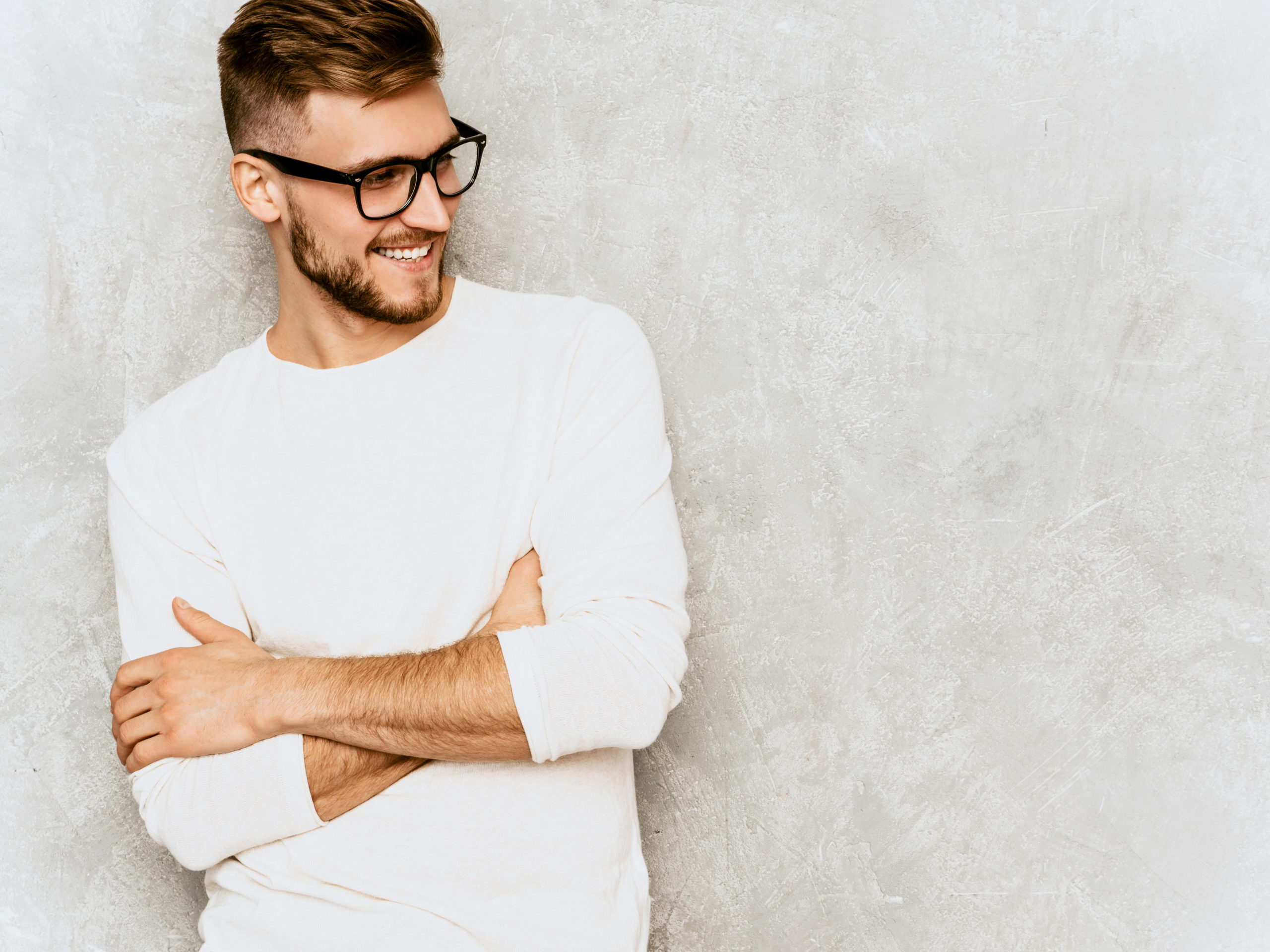  Portrait of handsome smiling hipster lumbersexual businessman model wearing casual summer white clothes and spectacles. Fashion stylish man posing against gray wall